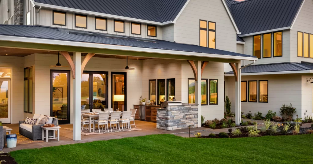 The back of a home facing a large covered patio with a living area, a dining area with a large table, and a kitchen area.