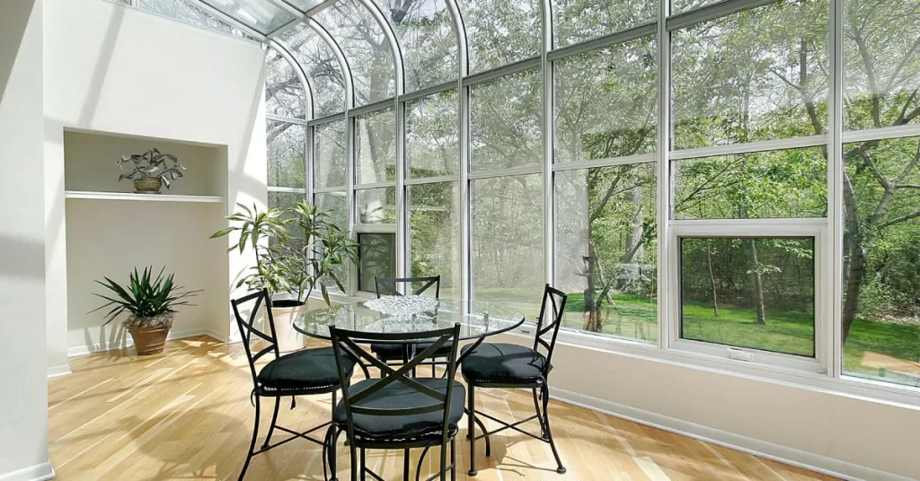 A sunroom with nearly floor-to-ceiling windows with hardwood flooring, white walls, and a black dining room set.