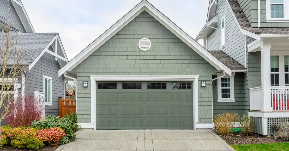 A green A-frame garage is attached to a matching two-story home with white accents and a front porch.