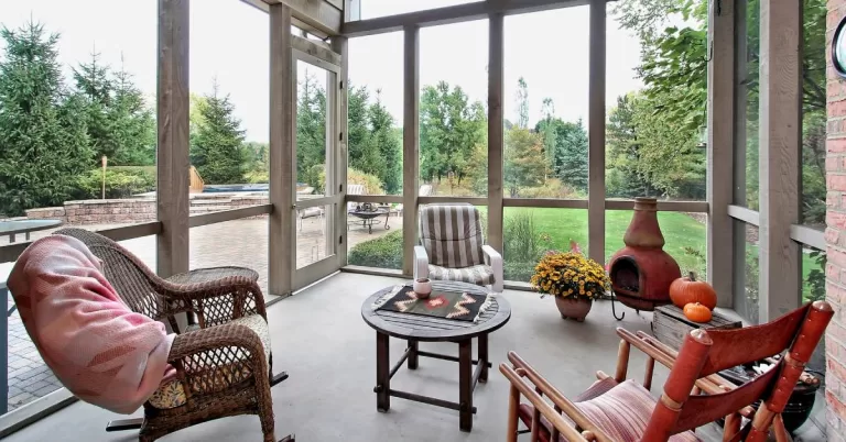 An A-frame screened porch with three different chairs and a round table in the center overlooking a large backyard.