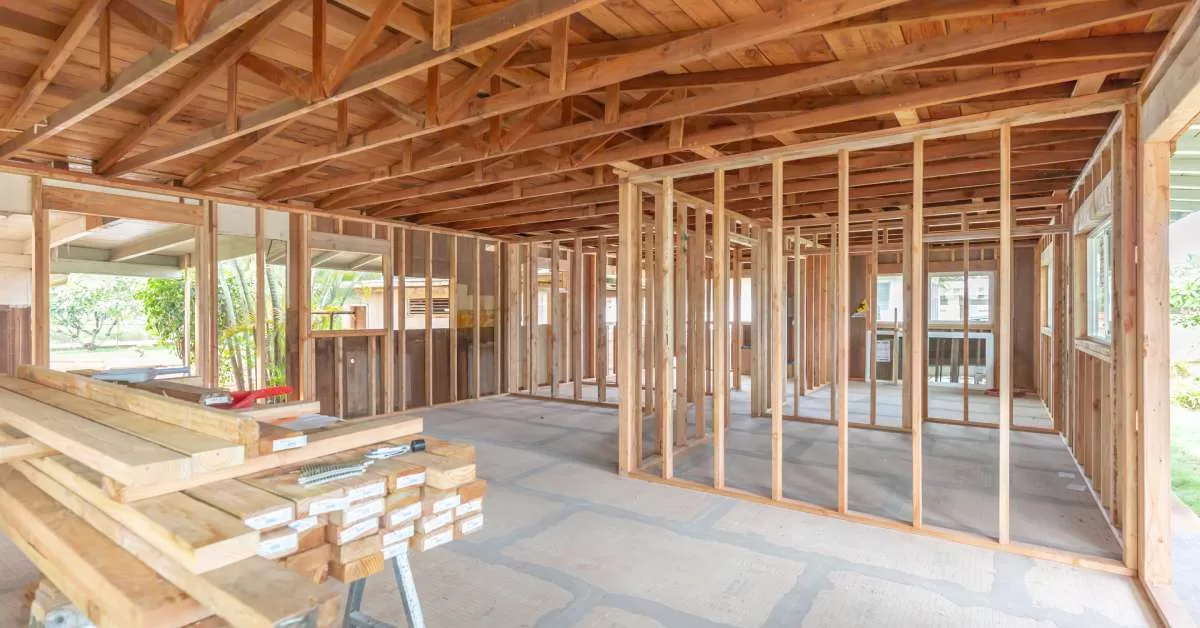 A home under construction on a sunny day with an exposed wood frame and a table of unused wood beams to the side.