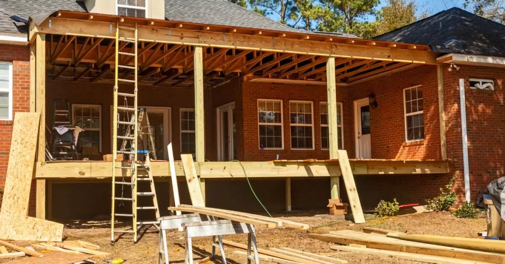 A backyard covered patio under construction attached to a brick two-story house with an exposed wood frame.