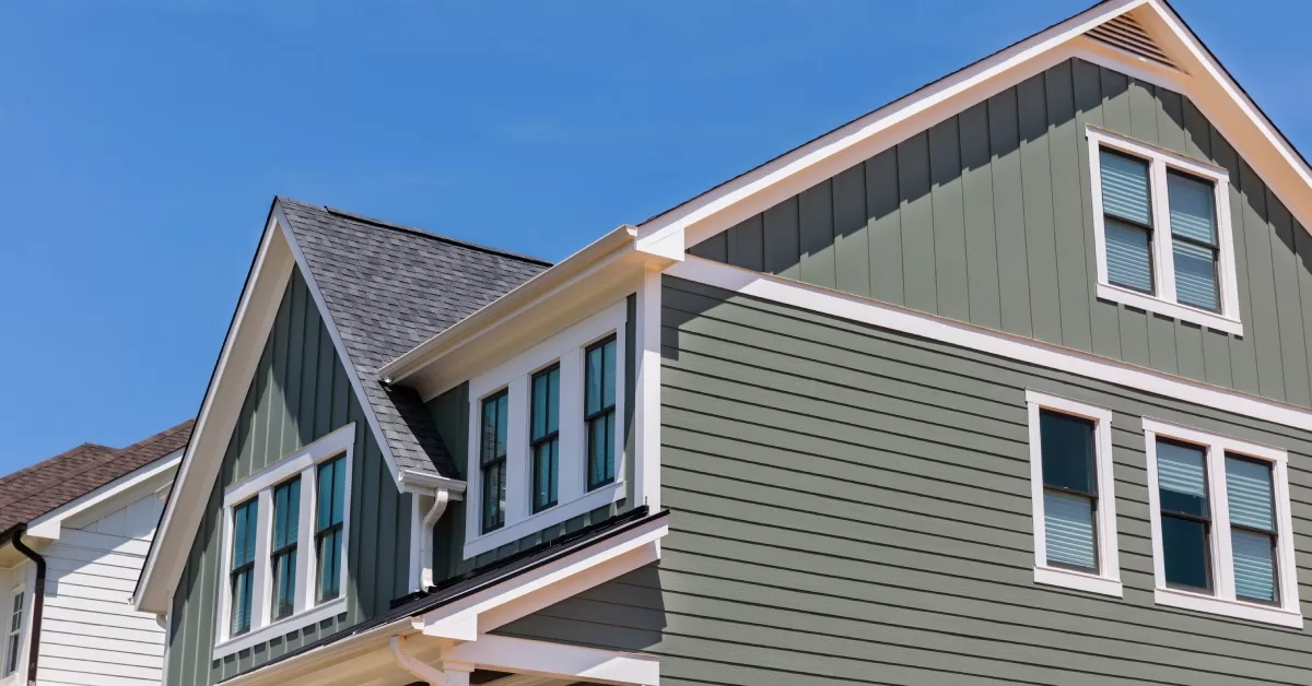 A two-story home with green, wood horizontal siding, white trim, and a shingle roof with several windows.