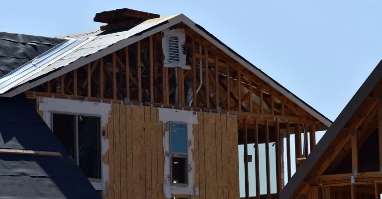 A two-story home with green, wood horizontal siding, white trim, and a shingle roof with several windows.