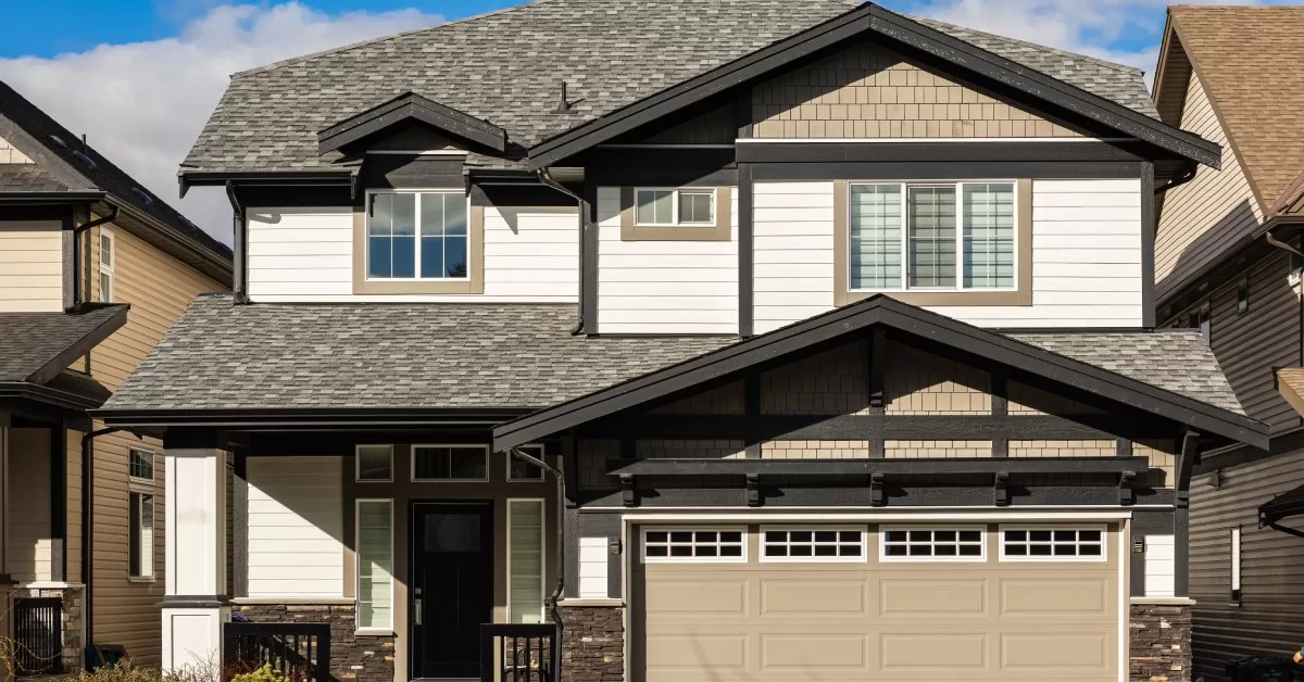 A two-story suburban house with stone and white wood siding, shingle roof, and attached garage with a beige door.