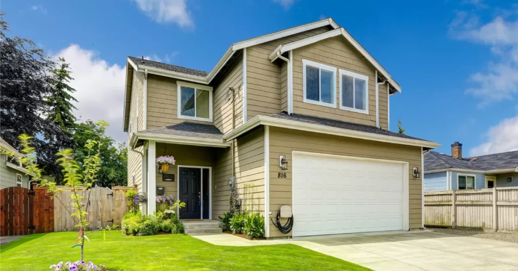 A two-story suburban house with beige wood siding, an attached garage with a single white door, and trimmed front lawn.