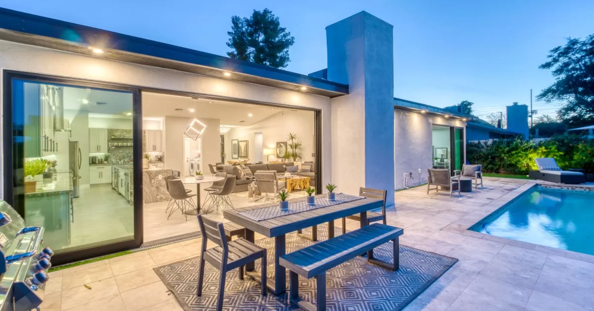 A modern house with a large glass sliding door transitioning the kitchen and dining rooms to the backyard with a pool.