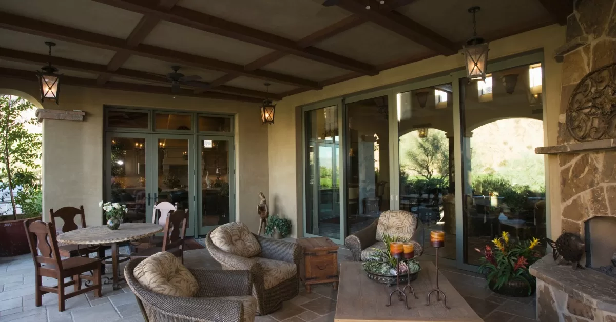 A Tuscan-inspired covered porch with a circular table and chairs, a seated area around a fireplace, and hanging lanterns.