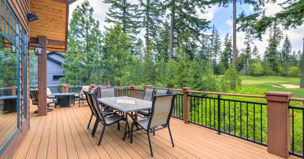 A large wood deck with a dining set surrounded by six chairs. The deck overlooks tall trees and a golf course.