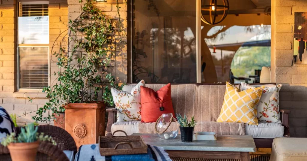 A rustic-inspired backyard patio with an outdoor couch, coffee table, two ottomans, and small potted cacti.