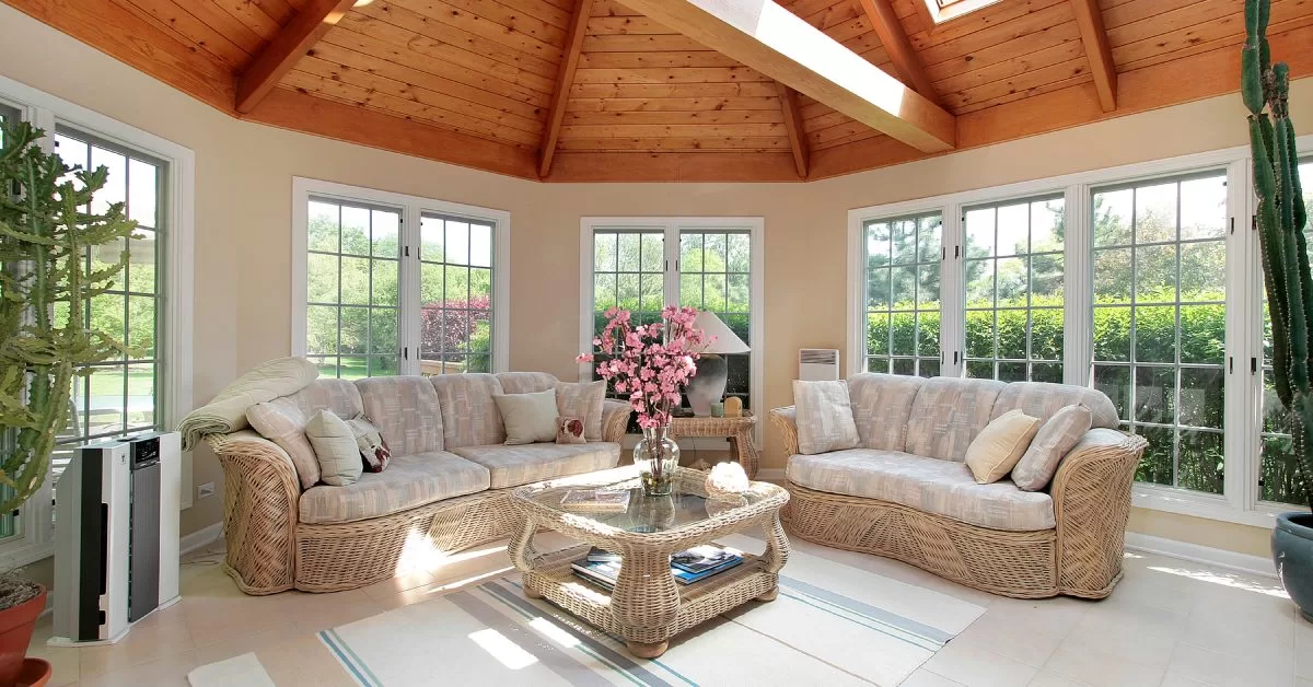 A round sunroom with vaulted wood panel ceiling, several paned windows, and a matching wicker furniture set.