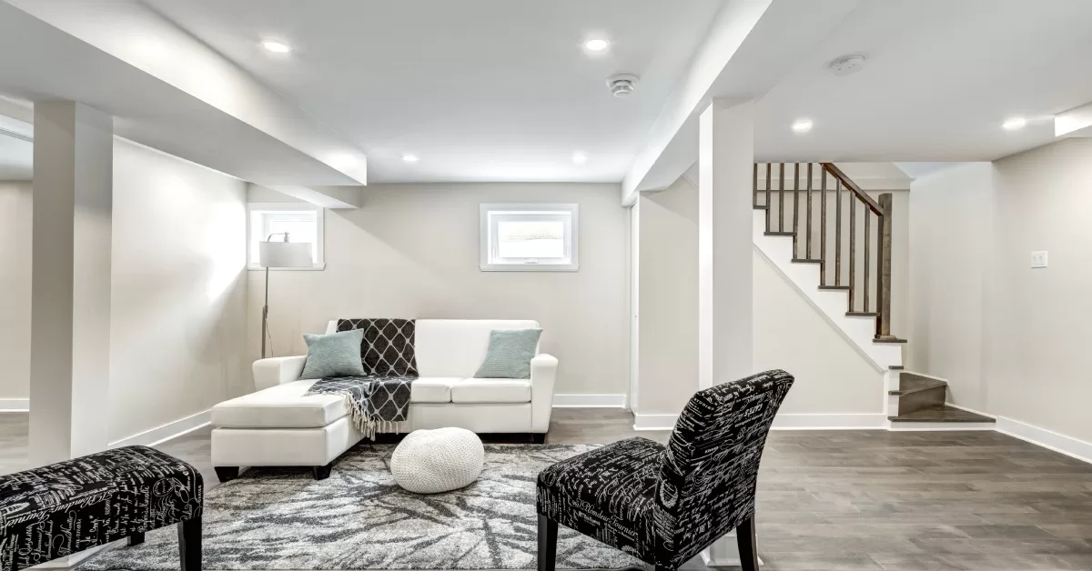 A finished basement with a furnished living area and staircase. The living area features a couch, two chairs, and a rug.