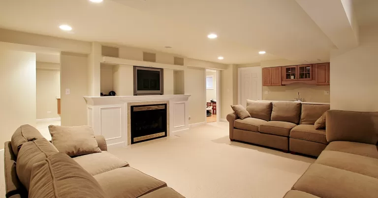 A spacious finished basement living area with a large sectional couch, fireplace with mounted TV, and wet bar.