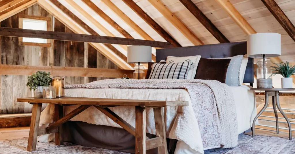 A rustic bedroom with wood-paneled ceilings and vertical beams. A bed with two side tables is in the room's center.