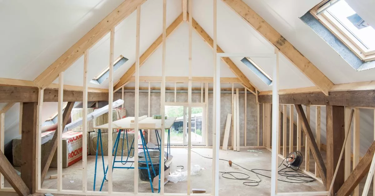 An in-progress home renovation with exposed vertical wood beams, an unfinished floor, and a work table.