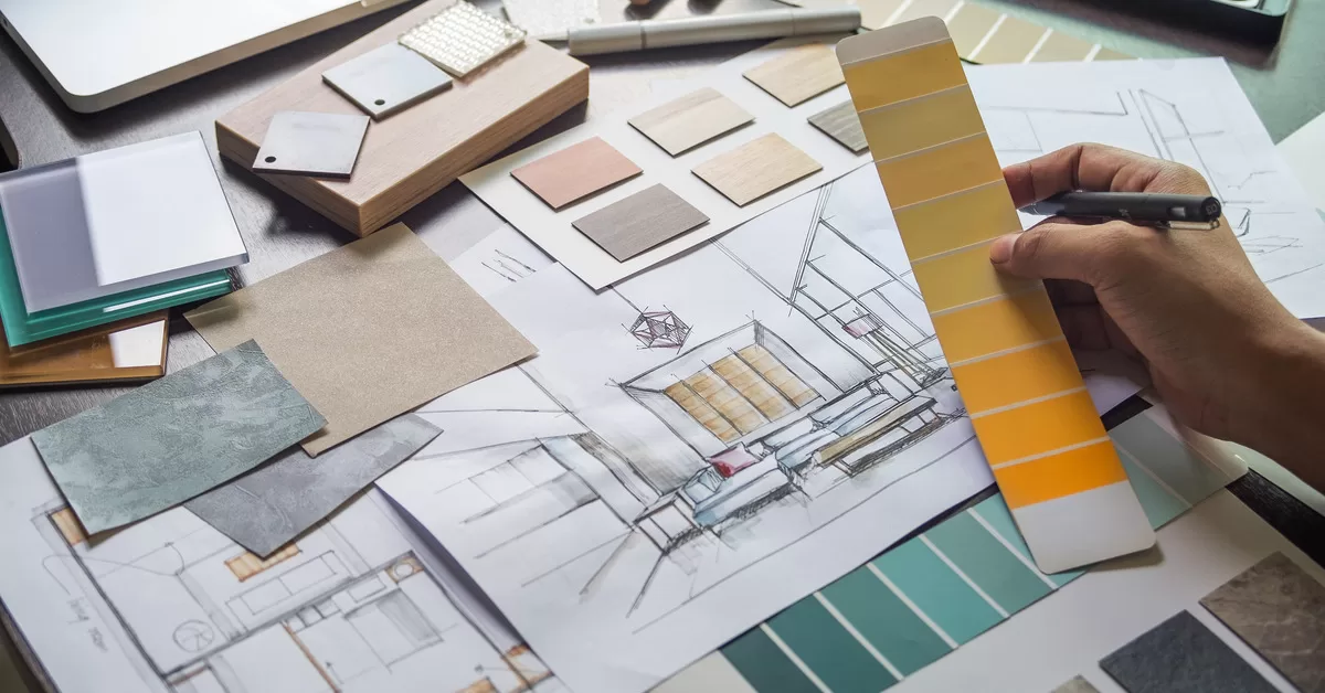 A spread of sketches of home interiors and paint and material samples. A designer holds a paint swatch with shades of yellow.