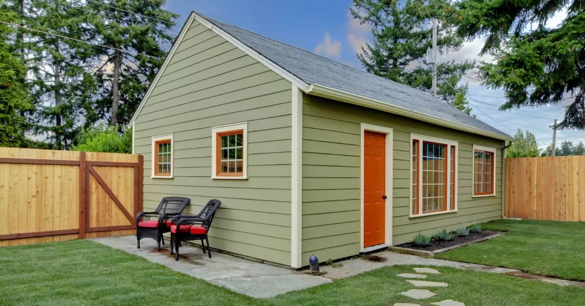 A light green accessory dwelling unit (ADU) in a grassy backyard. Stone pavers lead to the orange front door.