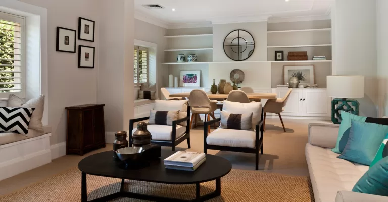 A living room and dining area with modern furniture. The back wall has built-in shelves displaying decor and cabinets.