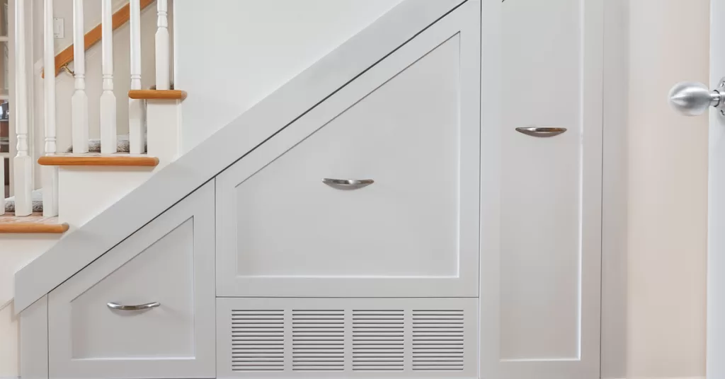 Three light gray pullout cabinets of varying sizes with metal handles under a staircase with wood railing.