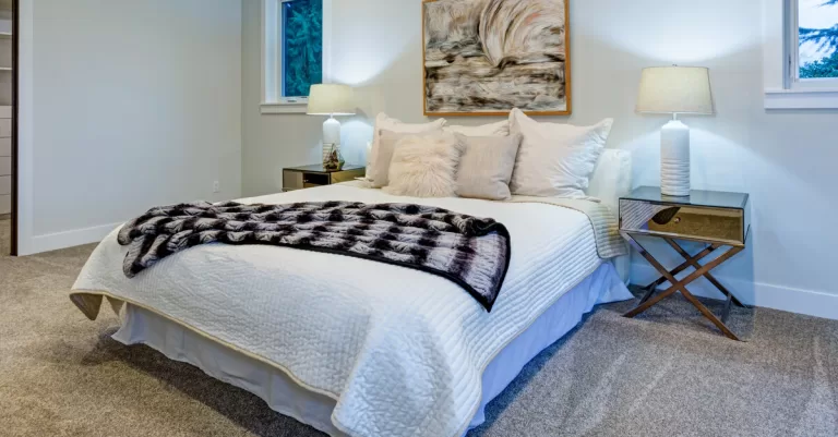 A guest bedroom with a made bed which has two side tables with lit lamps and a window on each side of the bed.