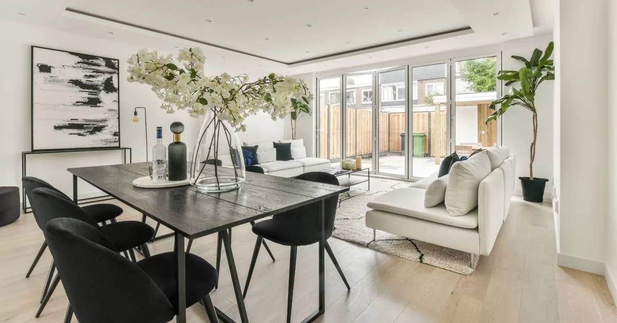 A contemporary home interior with a dining table, two couches facing each other, and multiple glass doors shining light in.