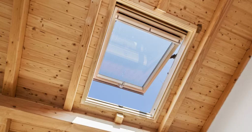 A wood panel ceiling with an open skylight facing a blue sky allowing natural light to shine into the home.